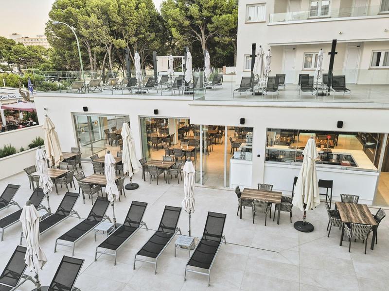 Espace extérieur moderne d'un hôtel avec chaises longues et tables sur une terrasse.