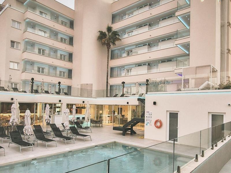 Bâtiment d'hôtel moderne avec piscine extérieure et chaises longues en plein jour.