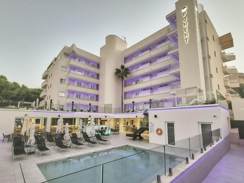 Hôtel moderne avec piscine, transats et balcons entourés d'arbres au crépuscule.