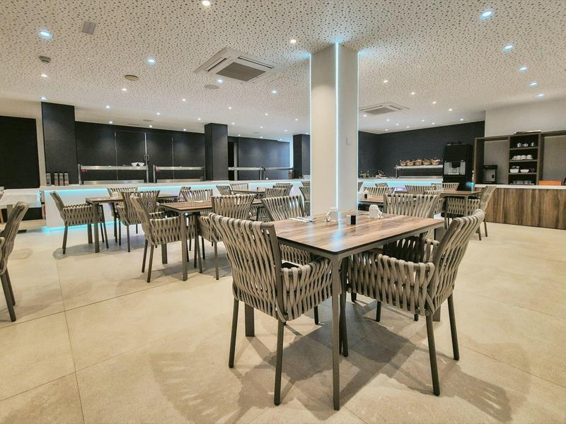 Salle à manger moderne avec tables et chaises, sol clair et éclairage au plafond