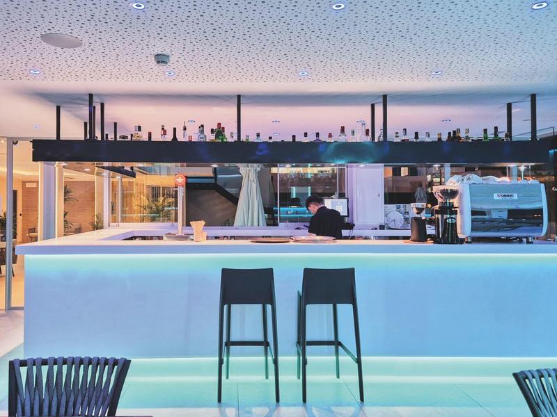 Espace bar d'hôtel moderne avec comptoir éclairé, tabourets hauts et éclairage élégant.