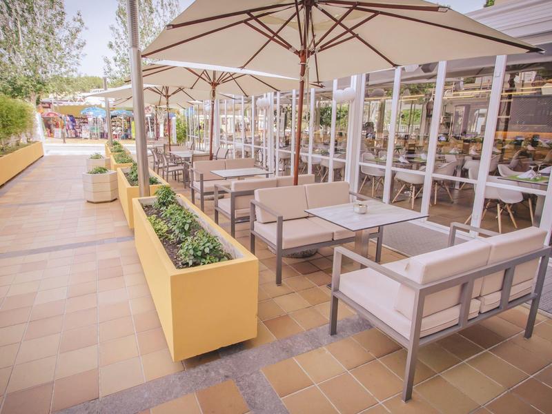 Espace extérieur d'un café avec tables, fauteuils et parasols le long d'un chemin.