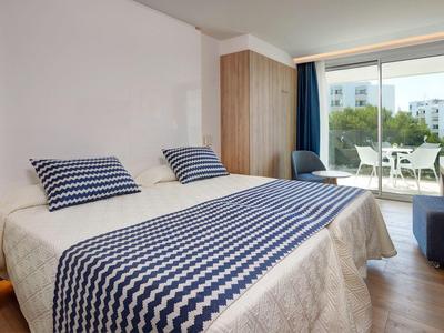 Habitación de hotel luminosa con cama doble, cojines azules y ventana grande con vista exterior.