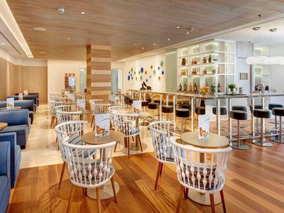 Moderner Hotel-Loungebereich mit Holzfußboden, gemütlichen Sesseln und einer Bar im Hintergrund.