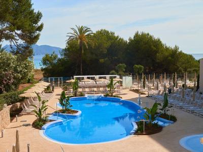Área de piscina con sombrillas y tumbonas rodeada de árboles y montañas al fondo