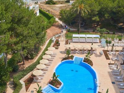 Gran piscina con palmeras y tumbonas junto a una playa de arena concurrida y mar azul.