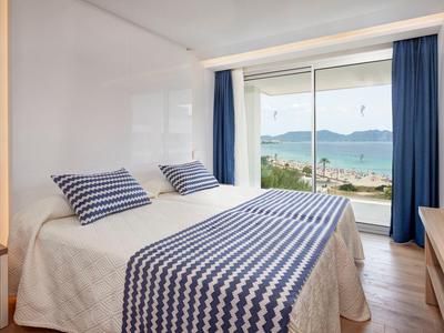 Dormitorio con luz natural, cama doble y vista al mar a través de grandes ventanas.