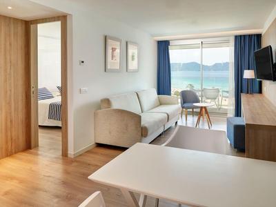 Sala de estar luminosa con sofá, TV montada, mesa, y balcón con vista al mar.