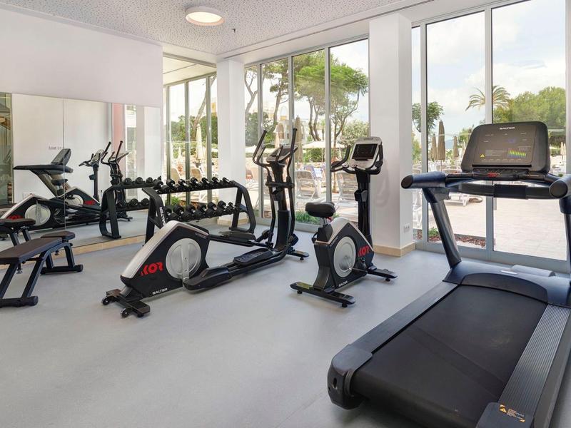 Gimnasio luminoso con equipos modernos y grandes ventanas que dan al exterior.