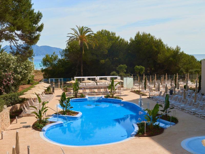 Área de piscina con sombrillas y tumbonas rodeada de árboles y montañas al fondo
