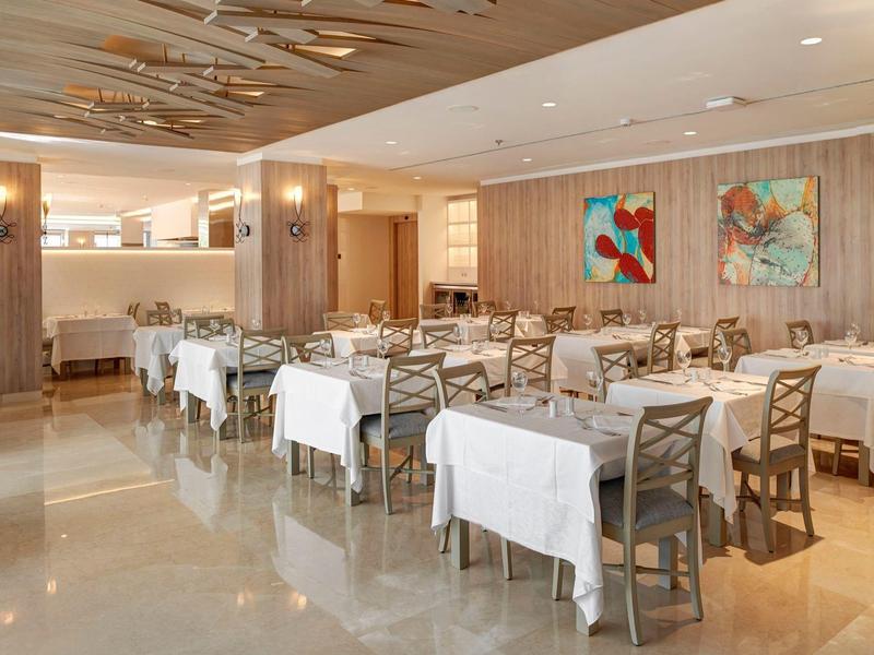 Comedor elegante de hotel con manteles blancos, sillas de madera y arte moderno en las paredes.
