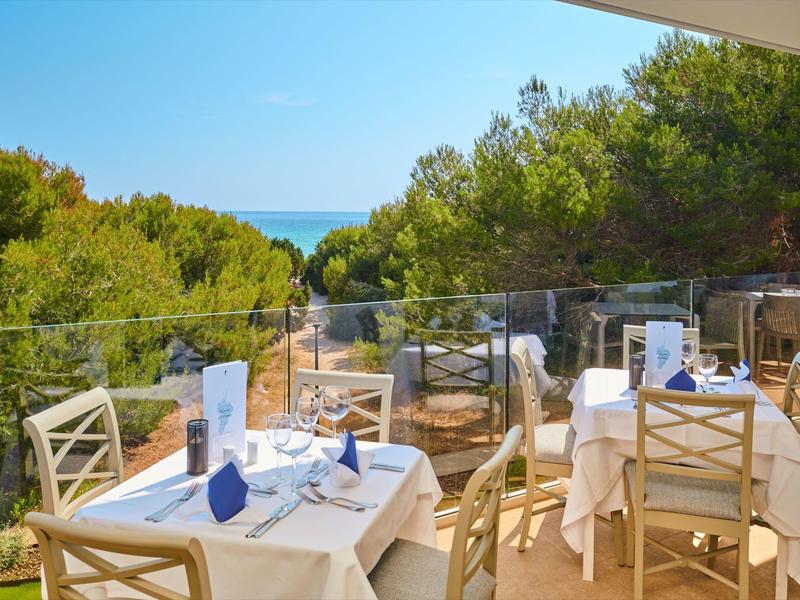 Mesas al aire libre con vista a árboles verdes y el mar en un día soleado.
