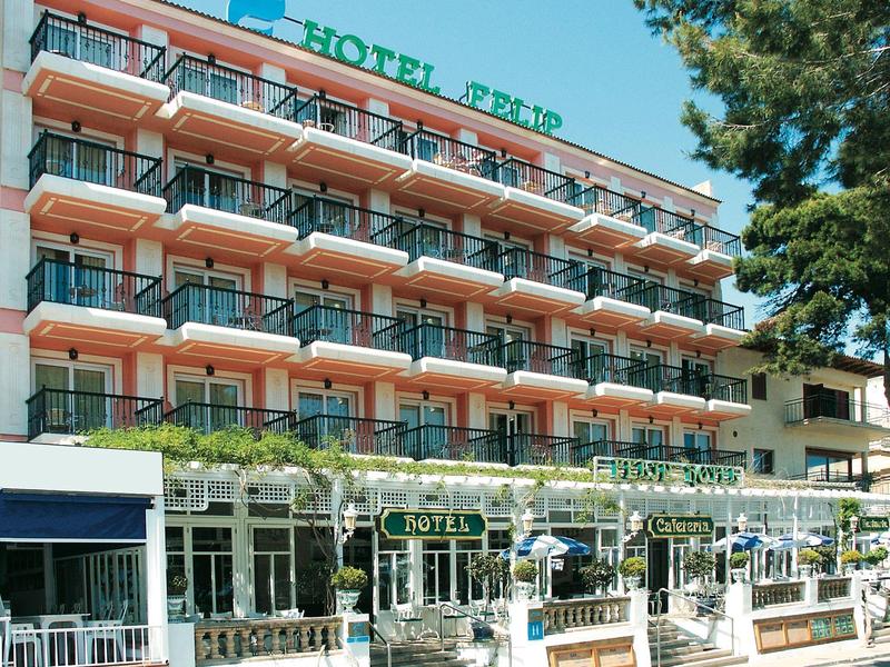 A multi-story hotel with balconies and outdoor seating surrounded by greenery under a clear sky.