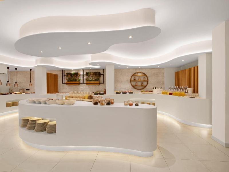 Spacious modern hotel buffet with curved white counters and warm lighting.