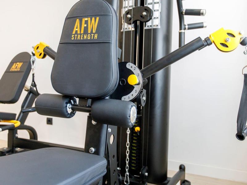 Black and yellow AFW Strength gym machine with adjustable arms and padded seat.