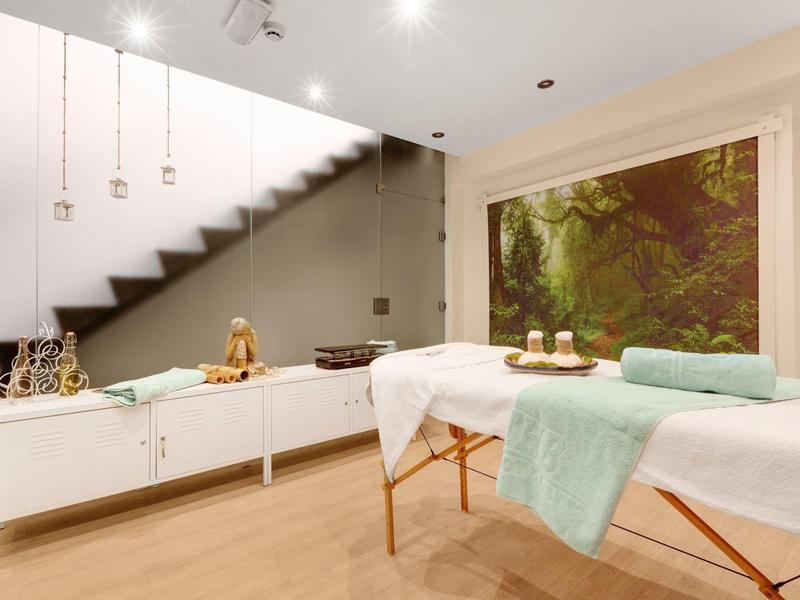 Modern spa room with massage table, soft towels, candles, and serene forest wall art.