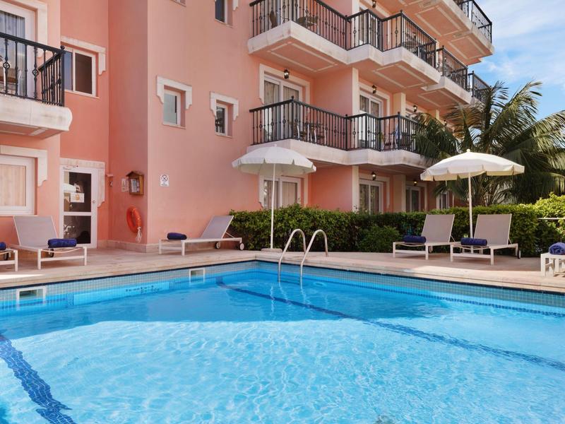 Outdoor pool beside a pink hotel building with sun loungers and umbrellas.