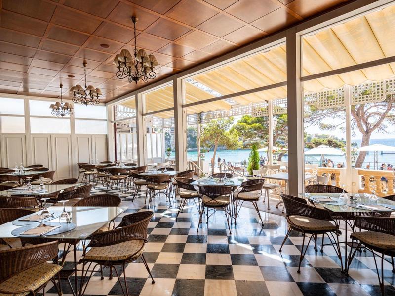 Spacious dining area with checkered floor, wooden ceiling, and large windows overlooking trees and water.