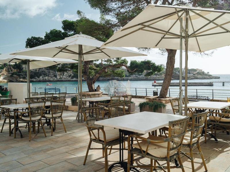 Outdoor seating area with tables, chairs, and large umbrellas near waterfront and trees.
