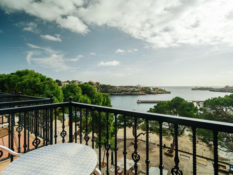 Balcony with a white table and black railing overlooking a beach and sea under a partly cloudy sky.