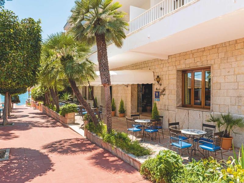 Buitenruimte van een hotel met tafels, stoelen en palmbomen langs een geplaveid pad.