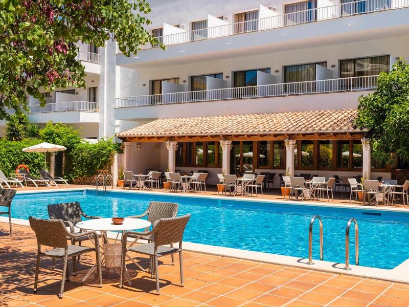 Hotelzwembad met parasols, stoelen en tafels in een zonnige binnenplaats.