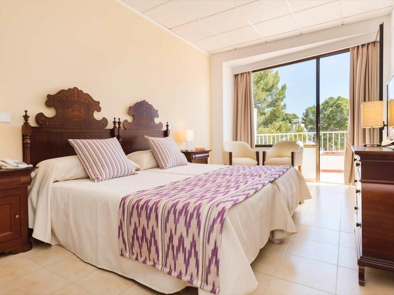 Gezellige hotelkamer met twee eenpersoonsbedden, houten meubels en balkon met uitzicht op groen.