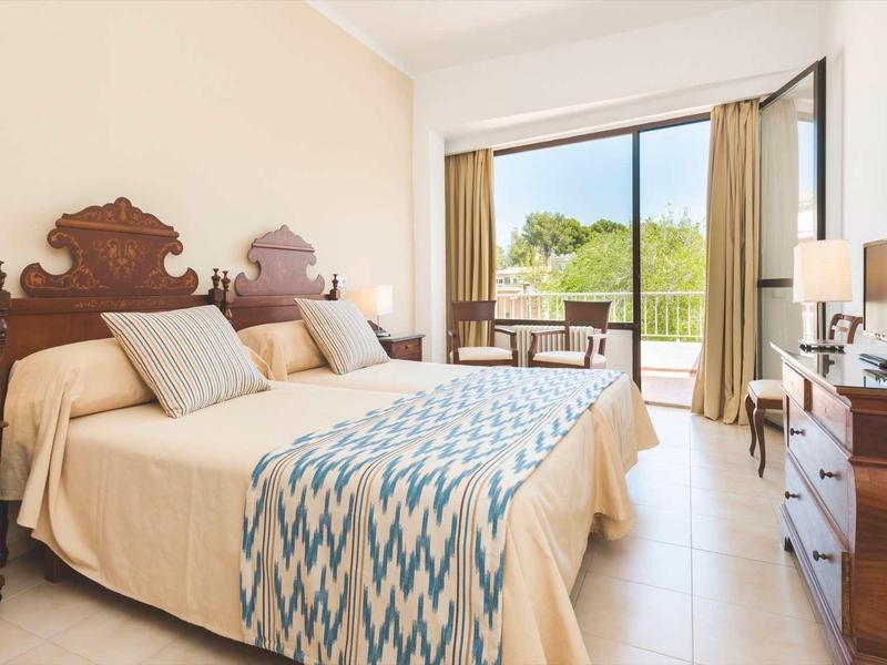 Lichte hotelkamer met twee bedden, houten meubels en balkon met uitzicht op groen.