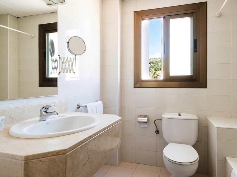 Lichte badkamer met wastafel, toilet, badkuip en raam met uitzicht naar buiten.