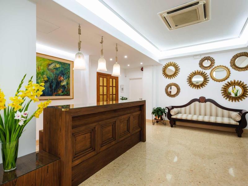 Lichte hotel lobby met houten balie, antieke bank en bloemstuk.