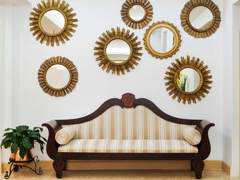 Elegant bank met gestreepte stof en meerdere ronde zonnespiegel op de muur erachter.