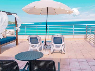 Terrasse mit Stühlen, Sonnenschirm und Meerblick in einem Hotel am Strand.