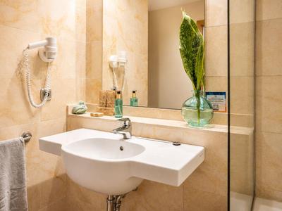 Modernes Badezimmer mit weißem Waschbecken, Haartrockner und grünem Blatt in Vase.