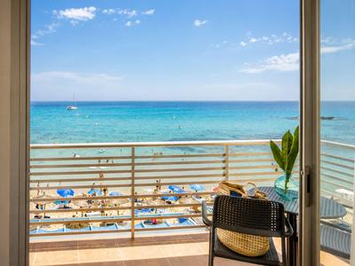 Blick vom Hotelbalkon auf Strand mit Sonnenschirmen und blauem Meer unter hellem Himmel.