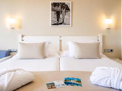 Zwei nebeneinander stehende Betten mit weißen Laken und Decken in einem hellen Hotelzimmer.
