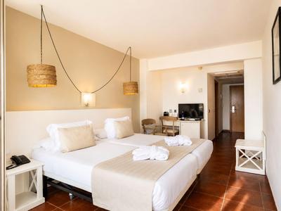 Helles Hotelzimmer mit Doppelbett, Holzfüßen und modernen Lamellenlampen an der Wand.