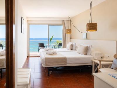 Helles Hotelzimmer mit Doppelbett, Sofa, Terrassentür und Blick auf das Meer.