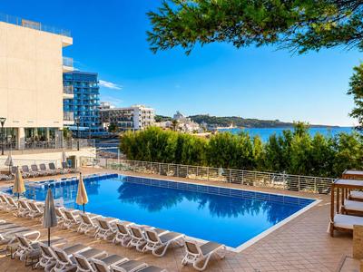 Moderner Hotelpool mit Liegestühlen und Meerblick unter blauem Himmel.