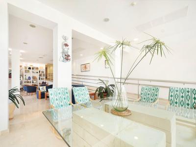 Helle, moderne Hotel-Lounge mit Glas-Tisch, gemusterten Stühlen und tropischen Pflanzen.