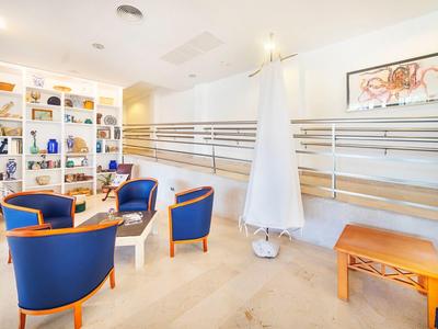 Heller Wartebereich mit blauen Sesseln, Holztisch und dekorativer Verkleidung an der Wand.