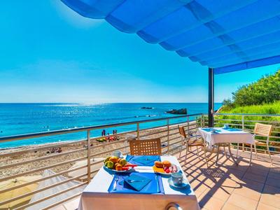 Balkon mit Tisch und Stühlen mit Meerblick und Strand unter blauem Himmel