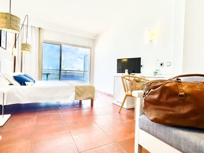 Helles Hotelzimmer mit großem Fenster, Bett und brauner Reisetasche auf dem Sofa.