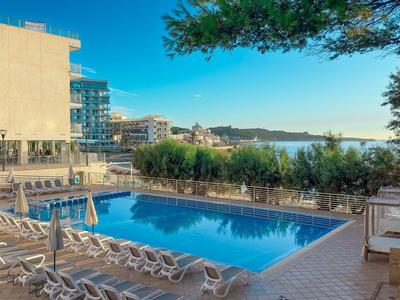 Hotelpool mit Sonnenliegen und Blick auf das Meer bei klarem Himmel