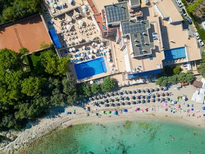 Vogelperspektive eines Strandes mit Sonnenliegen, blauem Pool und angrenzendem Hotelgebäude.