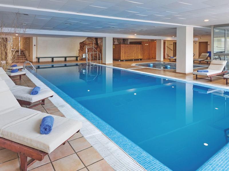 Innenhallenbad mit blauer Wasserfläche, Liegestühlen und Handtüchern auf dem Beckenrand