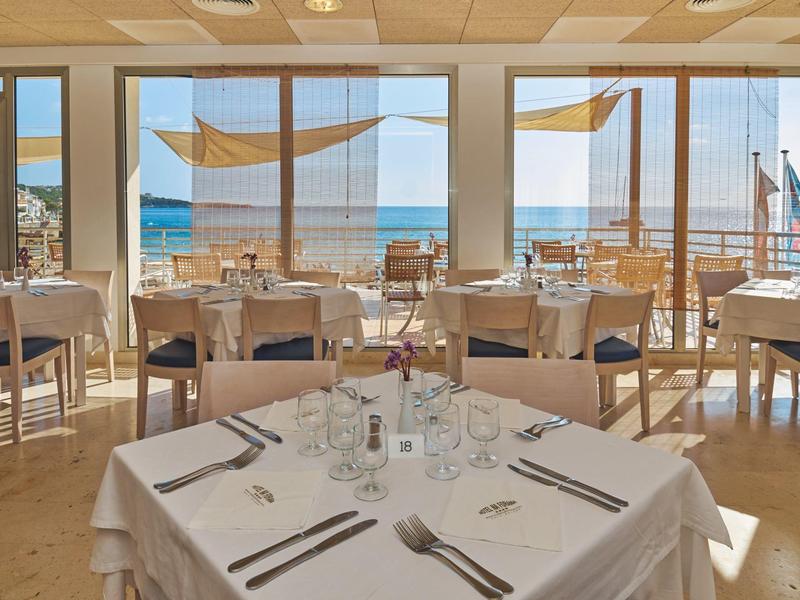 Heller Restaurantbereich mit Meerblick, gedeckten Tischen und Holzstühlen