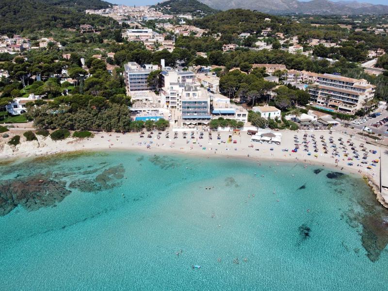 Blick auf einen Strand mit klarem türkisfarbenem Wasser und Hotels im Hintergrund.