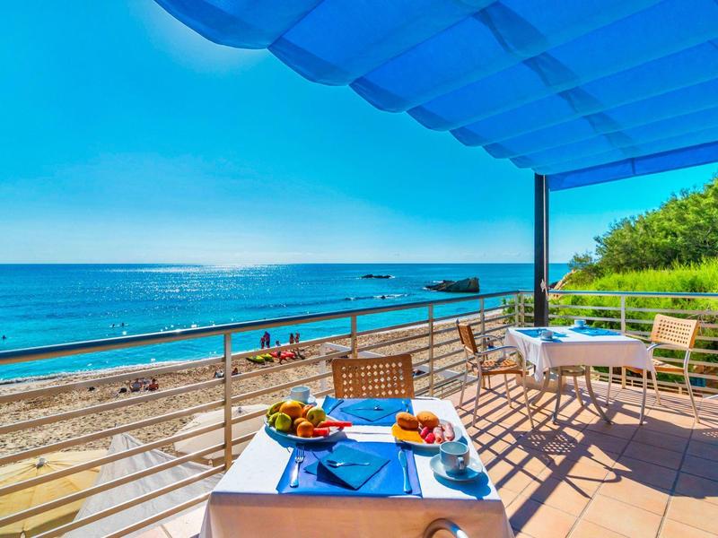 Balkon mit Tisch und Stühlen mit Meerblick und Strand unter blauem Himmel
