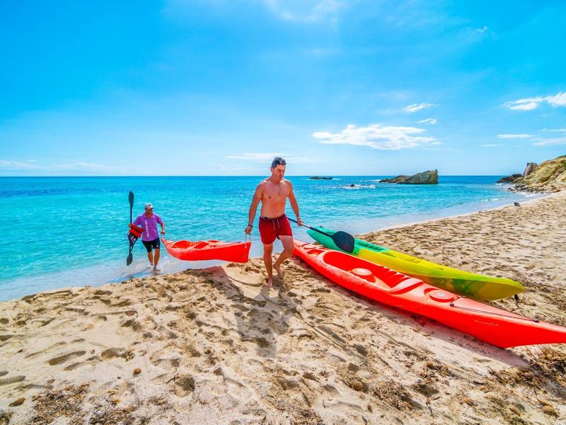 Zwei Männer ziehen Kajaks am sandigen Strand bei sonnigem Wetter ins Wasser.