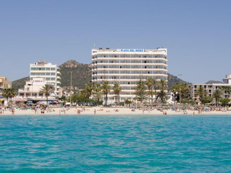 Beachfront hotels with white buildings and palm trees by clear blue water under a bright sky.